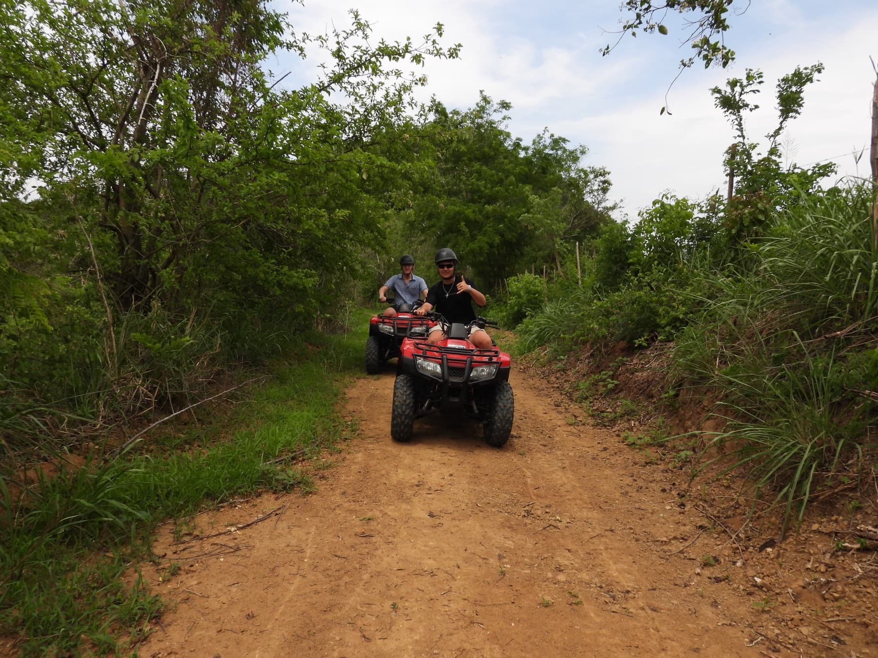 Dos visitantes en cuatrimotos rojas patrullando un sendero abierto de la reserva, uno saluda con el pulgar arriba