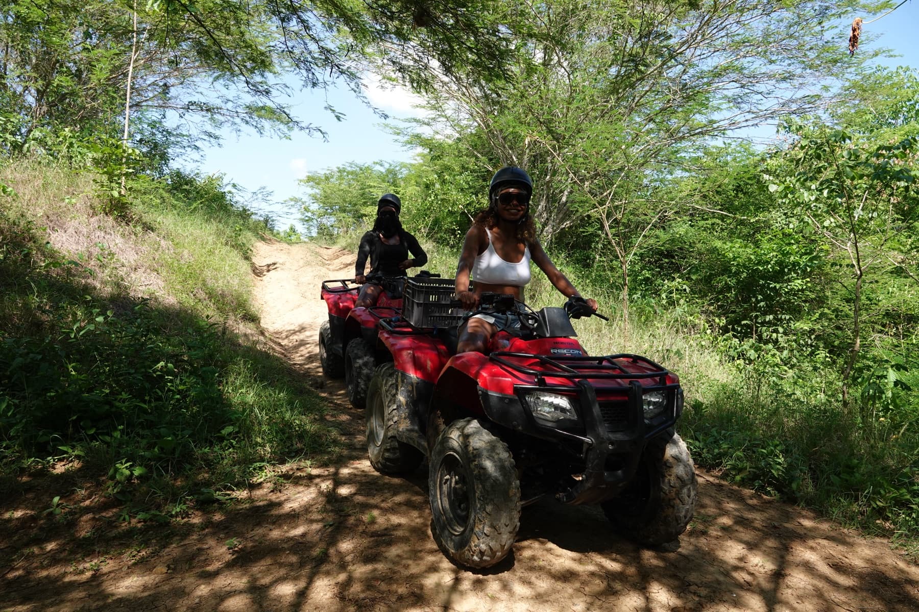 Dos visitantes en cuatrimotos bajando un sendero de colina entre árboles del bosque seco